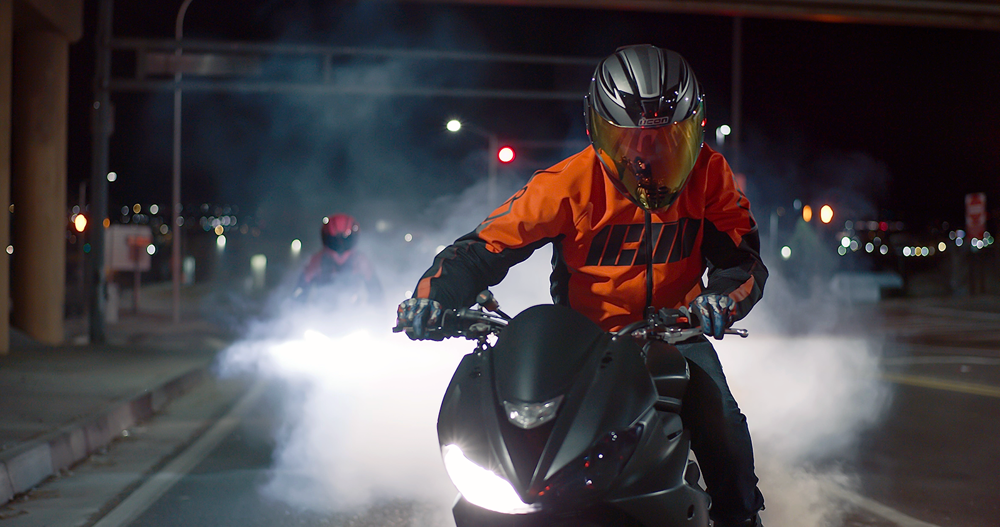 person riding a motorcycle at night wearing a bright orange reflective jacket