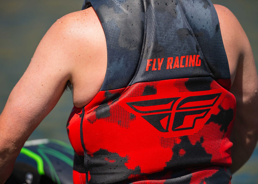 Close up image of a male wearing a red and black Fly life vest aboard his jet ski