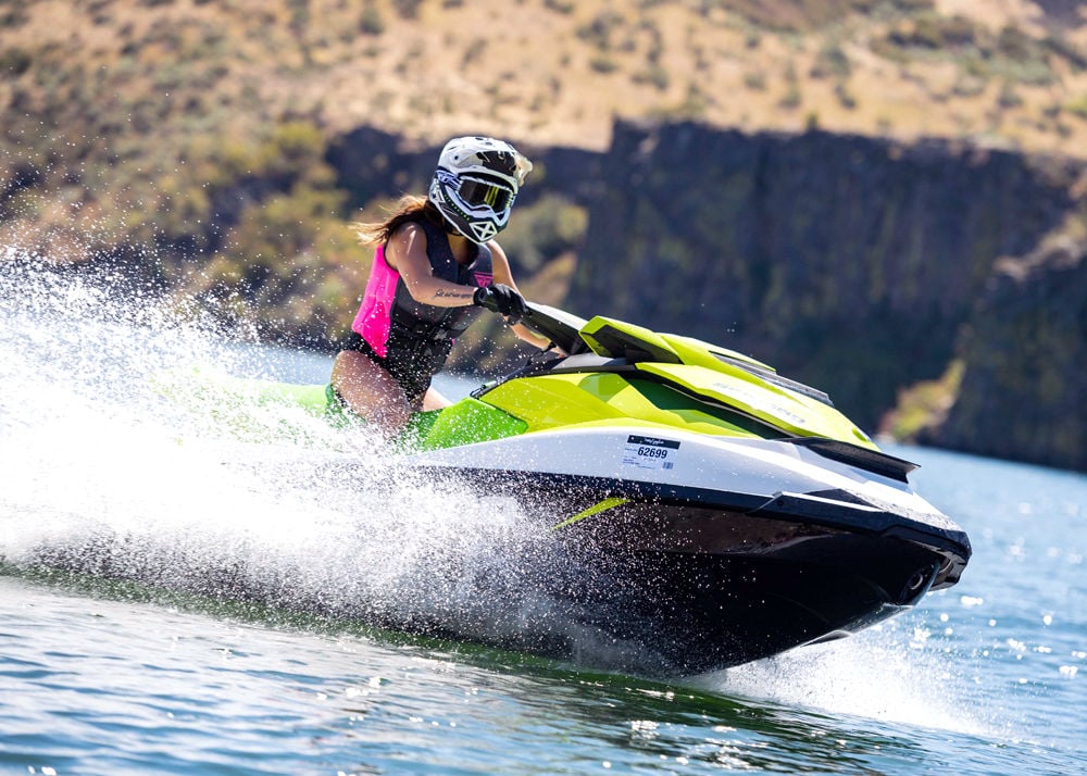 Young woman riding a bright yellow and white jet ski wearing a pink and black Fly life vest.