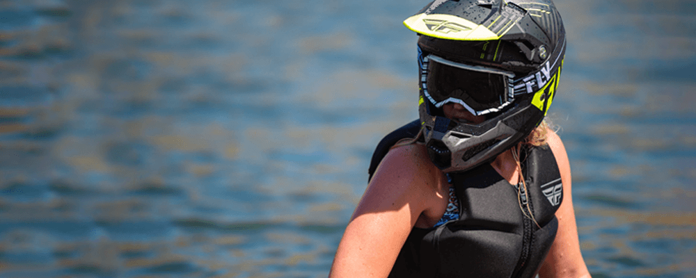 Woman riding a jetski wearing a helmet, goggles, and a life vest
