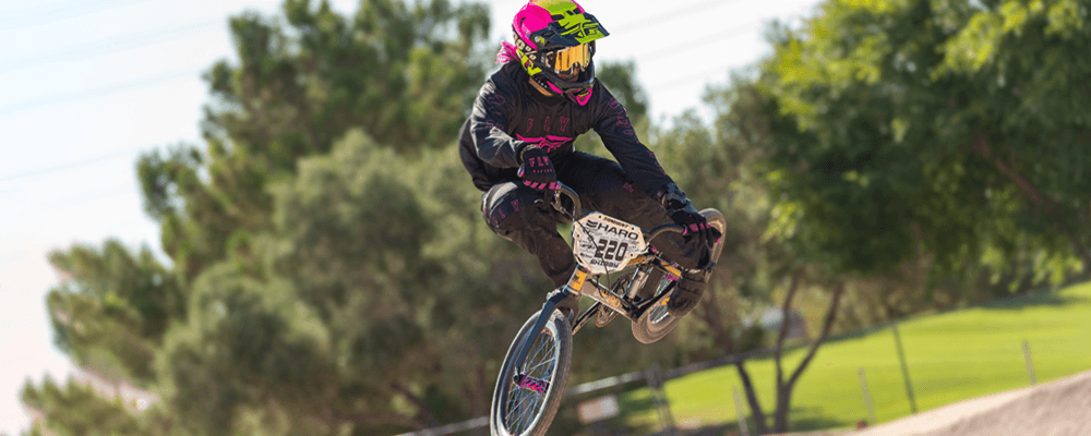 Person riding a BMX bike in a BMX park, fully geared in a helmet, goggles, and gloves