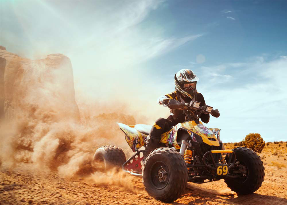 Person racing a modern-day ATV through the desert with dust blowing behind