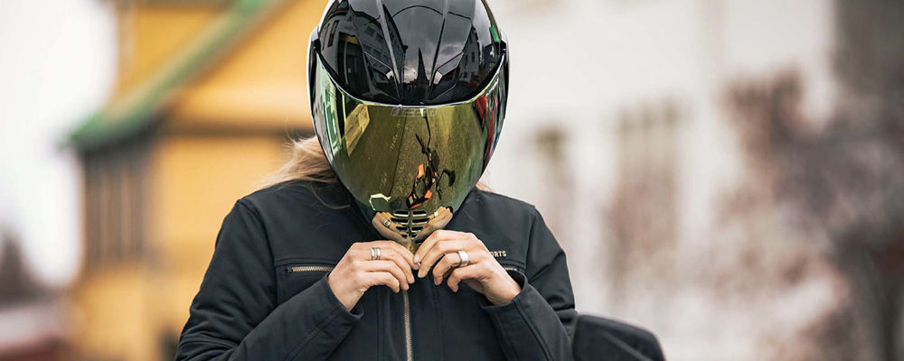 Woman closing the yellow mirrored face shield on her matte black helmet