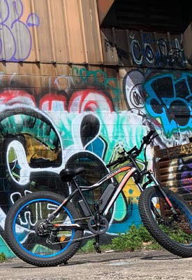 An Ecotric Rocket eBike parked in front of a wall of graffiti.